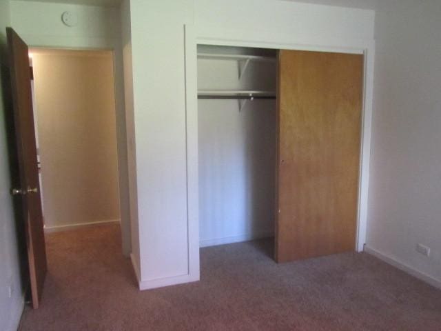 unfurnished bedroom with dark colored carpet and a closet