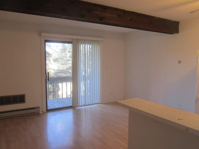 empty room featuring beamed ceiling, wood-type flooring, and a baseboard radiator