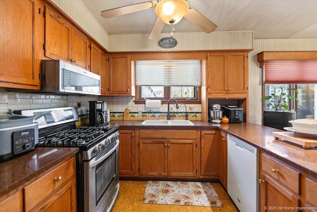 kitchen with stainless steel appliances, sink, ceiling fan, decorative backsplash, and dark stone counters