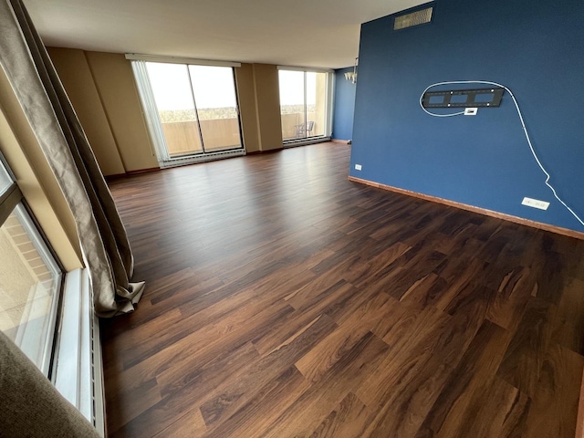 spare room featuring dark wood-style floors, expansive windows, baseboards, and a chandelier