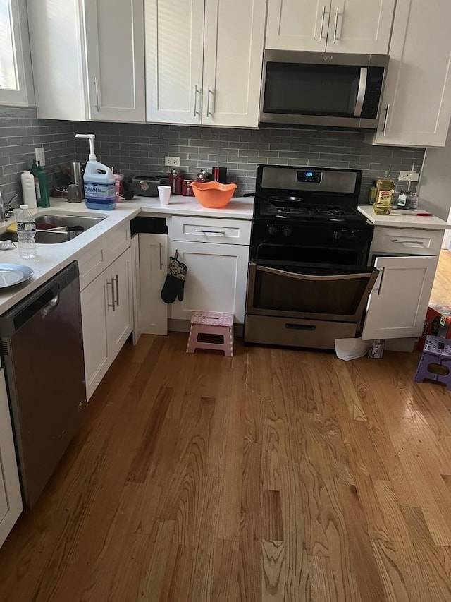 kitchen featuring appliances with stainless steel finishes, tasteful backsplash, white cabinetry, sink, and light wood-type flooring