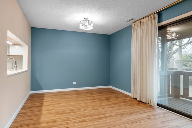 spare room with sink, light hardwood / wood-style floors, and a textured ceiling