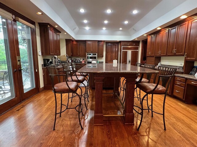 kitchen with paneled fridge, hardwood / wood-style flooring, a raised ceiling, and a kitchen island