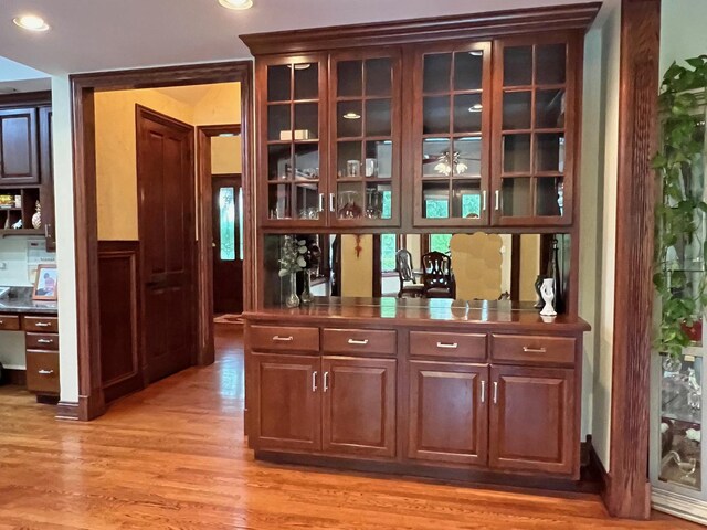 bar with dark brown cabinetry and light hardwood / wood-style flooring