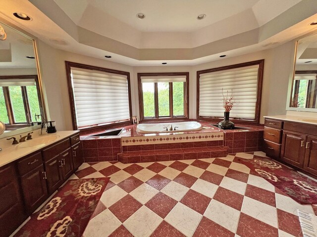 bathroom with a raised ceiling, tiled tub, and vanity