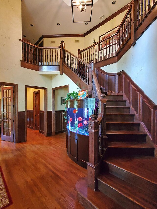 stairs featuring a chandelier, crown molding, wood-type flooring, and a high ceiling