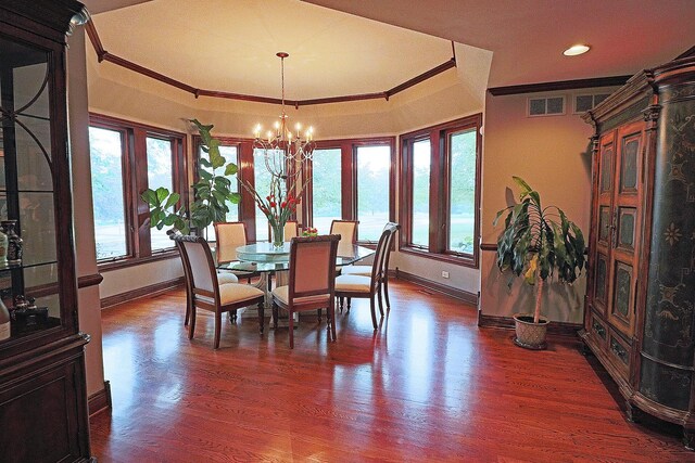 dining room with a raised ceiling, a notable chandelier, dark wood-type flooring, and crown molding