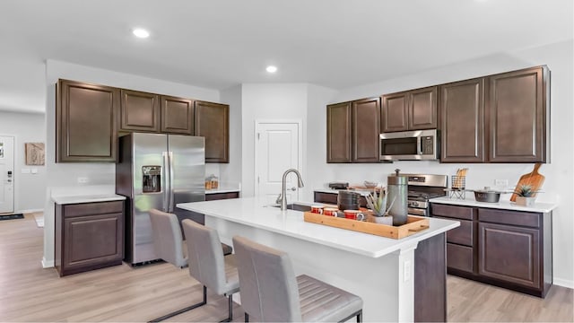 kitchen featuring a center island with sink, stainless steel appliances, light hardwood / wood-style floors, dark brown cabinetry, and sink