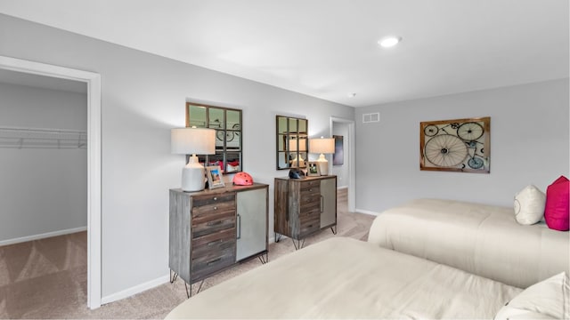 bedroom featuring a walk in closet, a closet, and light colored carpet