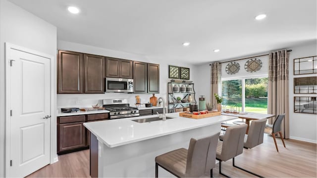 kitchen with sink, appliances with stainless steel finishes, light wood-type flooring, and a kitchen island with sink