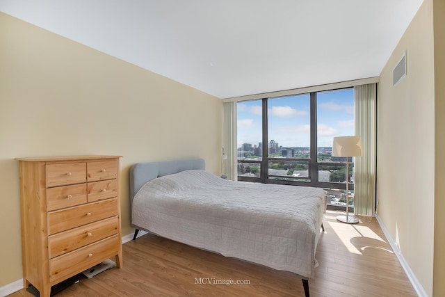 bedroom featuring baseboards, visible vents, floor to ceiling windows, and wood finished floors