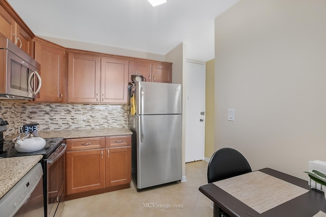 kitchen featuring light tile patterned floors, light stone counters, stainless steel appliances, decorative backsplash, and brown cabinets