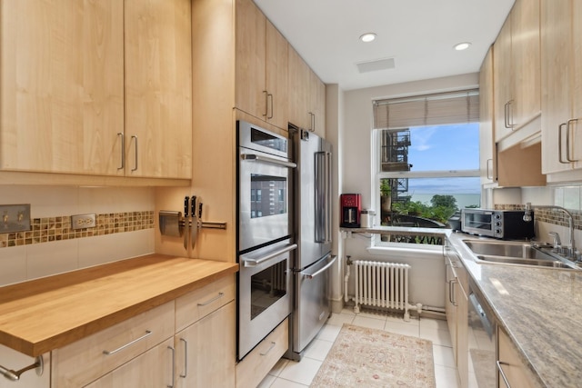 kitchen featuring sink, radiator, stainless steel appliances, light tile patterned floors, and light brown cabinetry