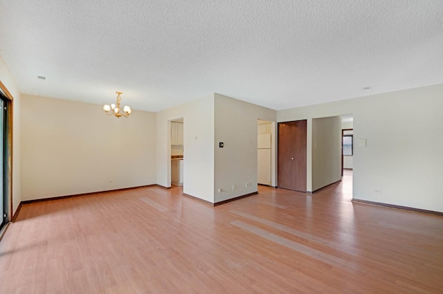 empty room featuring a chandelier, a textured ceiling, and light hardwood / wood-style floors