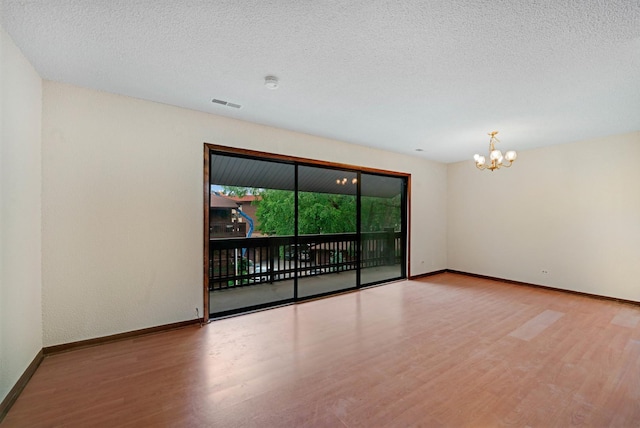 unfurnished room featuring hardwood / wood-style floors, a textured ceiling, and an inviting chandelier