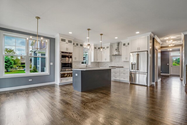 kitchen with hanging light fixtures, white cabinetry, stainless steel appliances, and wall chimney exhaust hood