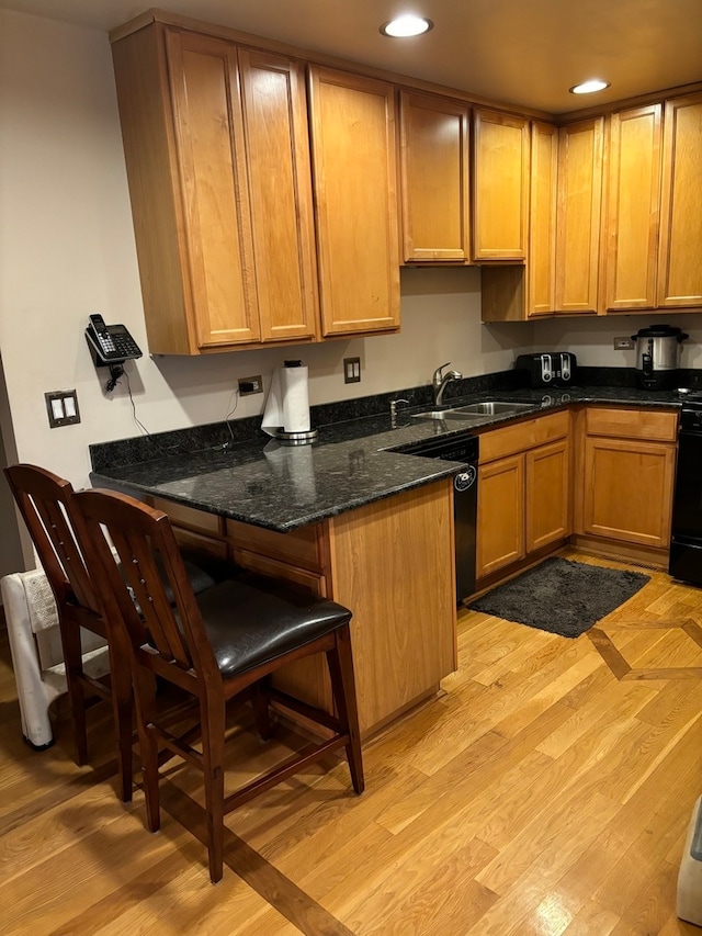 kitchen with dark stone countertops, dishwasher, light hardwood / wood-style floors, a kitchen breakfast bar, and sink