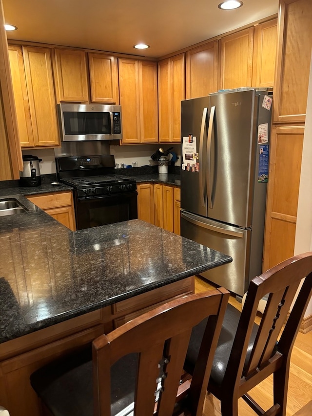 kitchen with dark stone counters, stainless steel appliances, light hardwood / wood-style floors, and a kitchen bar