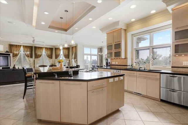 kitchen featuring tasteful backsplash, light brown cabinetry, a tray ceiling, sink, and a kitchen island with sink