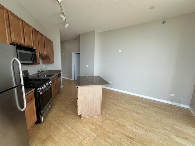 kitchen featuring sink, a center island, stainless steel appliances, track lighting, and light wood-type flooring