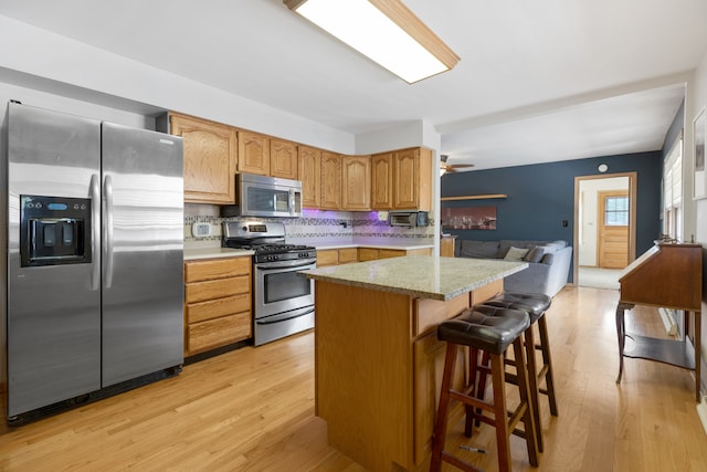 kitchen with ceiling fan, stainless steel appliances, decorative backsplash, light hardwood / wood-style floors, and a kitchen breakfast bar