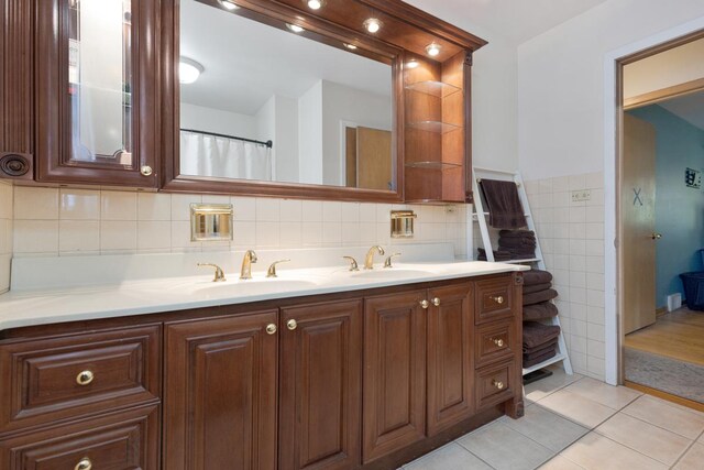 bathroom featuring dual bowl vanity, tile patterned flooring, backsplash, and tile walls