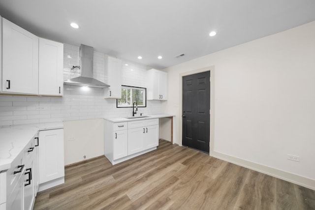 kitchen with white cabinets, backsplash, wall chimney exhaust hood, light hardwood / wood-style flooring, and sink