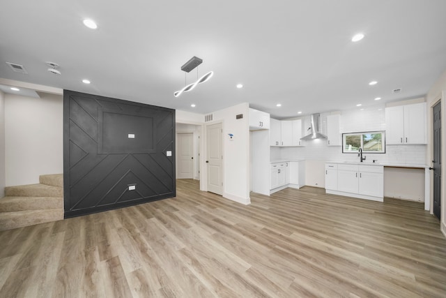 kitchen with hanging light fixtures, light hardwood / wood-style floors, white cabinetry, wall chimney exhaust hood, and sink