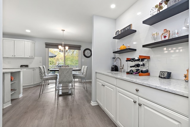 kitchen featuring an inviting chandelier, white cabinetry, sink, and light wood-type flooring