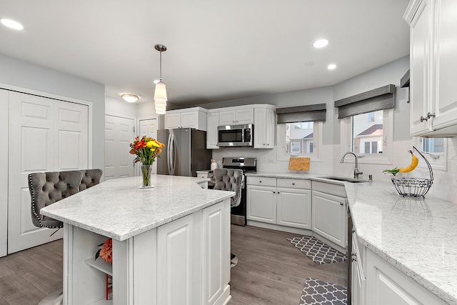 kitchen with appliances with stainless steel finishes, white cabinetry, sink, and decorative light fixtures