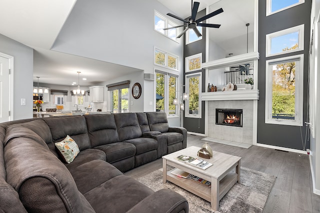 living room with a towering ceiling, hardwood / wood-style floors, ceiling fan with notable chandelier, and a tile fireplace