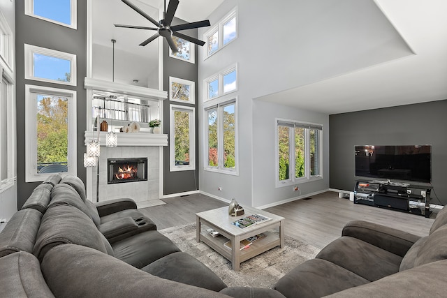 living room featuring a towering ceiling, a fireplace, light hardwood / wood-style floors, and ceiling fan