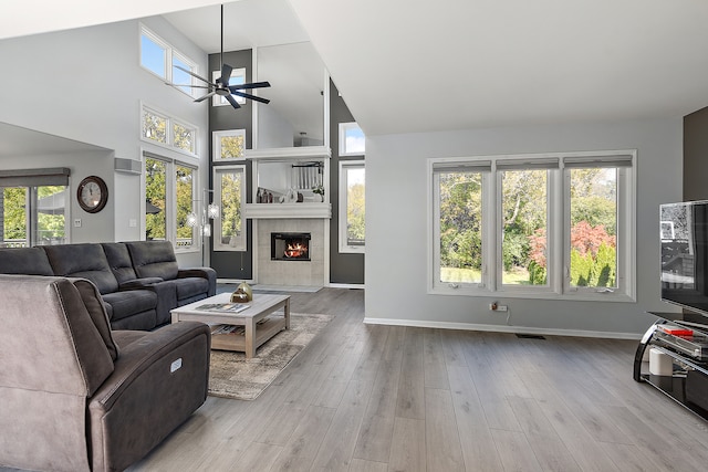 living room featuring light hardwood / wood-style floors, high vaulted ceiling, a tile fireplace, and ceiling fan