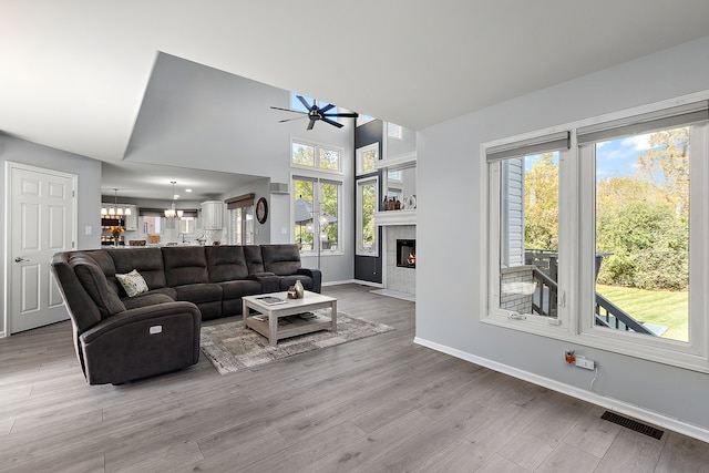 living room with a tiled fireplace, light wood-type flooring, and ceiling fan with notable chandelier