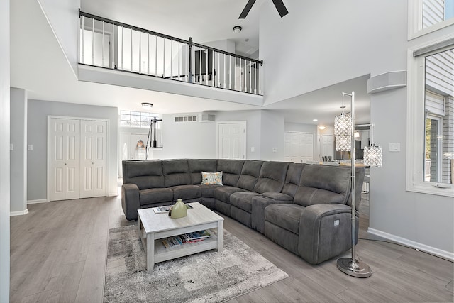 living room featuring wood-type flooring, a high ceiling, and ceiling fan with notable chandelier