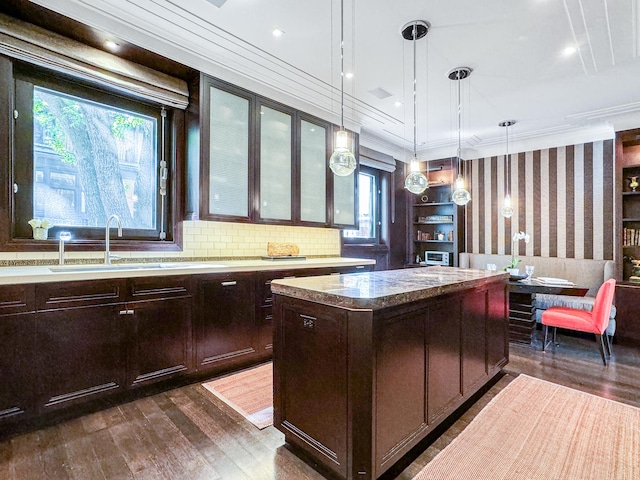 kitchen with dark wood-type flooring, ornamental molding, a sink, a center island, and wallpapered walls