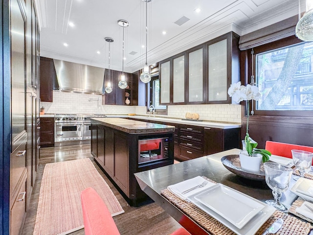 kitchen with dark brown cabinets, a center island, decorative backsplash, dark wood-style floors, and wall chimney exhaust hood