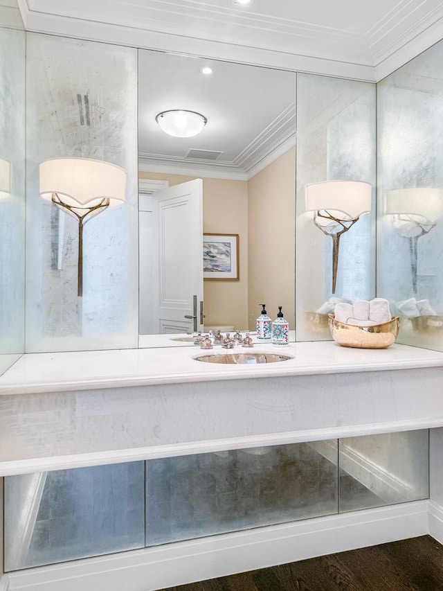 bathroom featuring wood finished floors, crown molding, and a sink