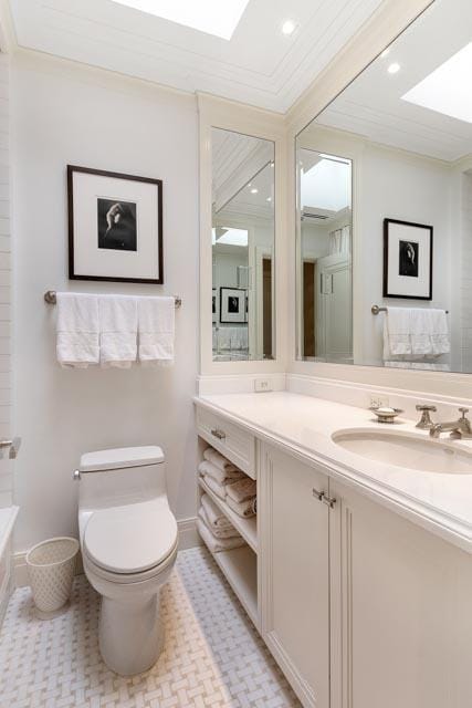 full bath featuring toilet, a skylight, vanity, and ornamental molding