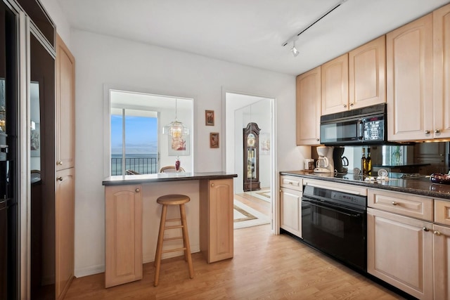 kitchen featuring a breakfast bar, pendant lighting, light brown cabinetry, light wood-type flooring, and black appliances