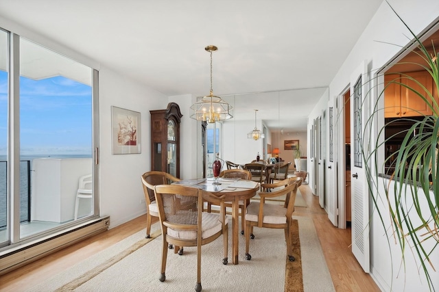 dining area with a notable chandelier, a baseboard radiator, a water view, light wood-style floors, and baseboards