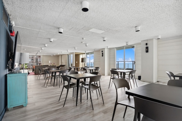 dining area featuring light wood finished floors, floor to ceiling windows, and a textured ceiling