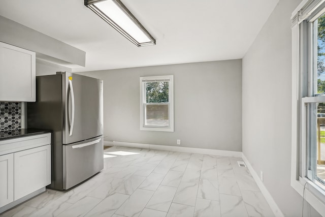 kitchen with plenty of natural light, stainless steel fridge, and white cabinetry