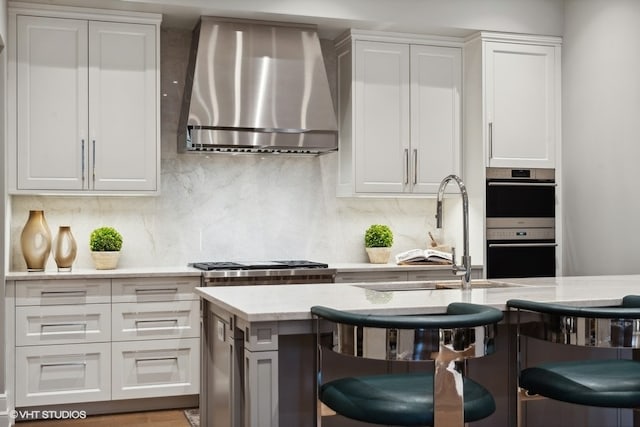 kitchen featuring a breakfast bar, double oven, decorative backsplash, and wall chimney range hood