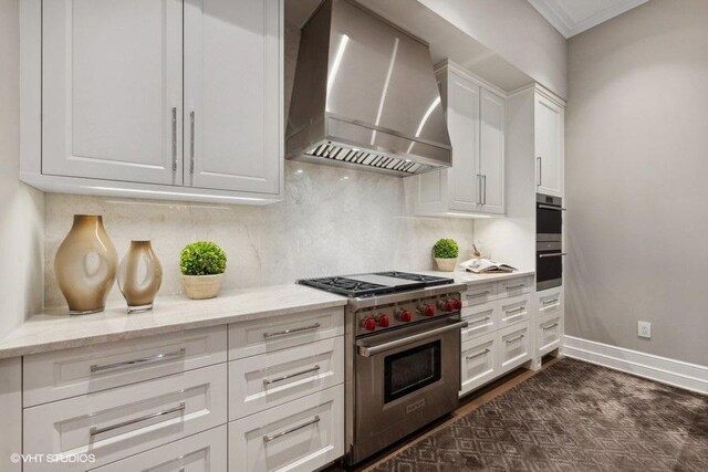 kitchen featuring stainless steel appliances, white cabinets, wall chimney range hood, decorative backsplash, and light stone countertops