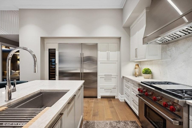 kitchen with high end appliances, white cabinetry, custom range hood, and light wood-type flooring