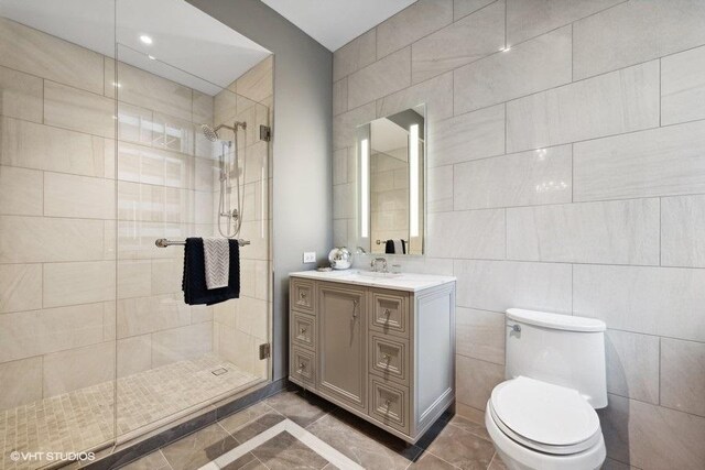 bathroom with tiled shower, toilet, vanity, tile walls, and tile patterned floors