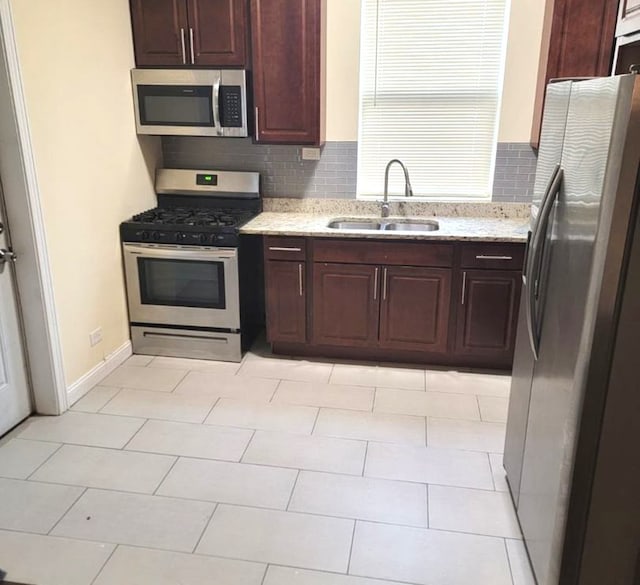 kitchen featuring light stone countertops, appliances with stainless steel finishes, tasteful backsplash, sink, and light tile patterned floors