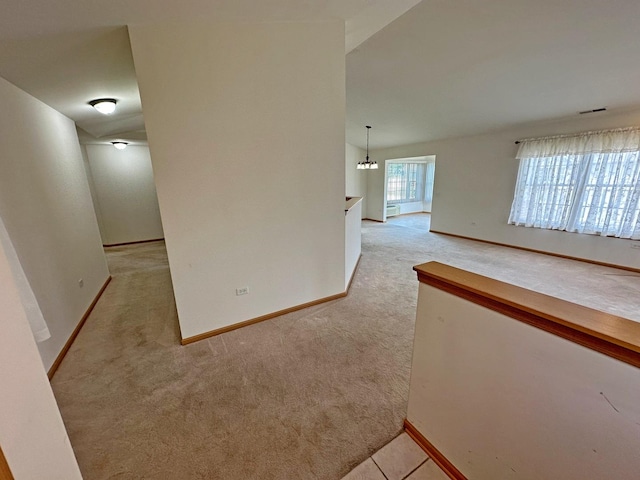 corridor featuring light colored carpet, baseboard heating, and an inviting chandelier