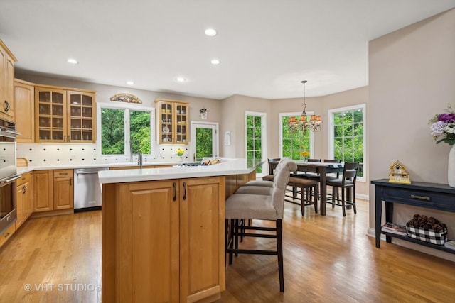 kitchen with a center island, tasteful backsplash, stainless steel dishwasher, decorative light fixtures, and light wood-type flooring